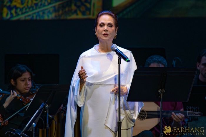 Parissa singing in a white embroidered robe, microphone at Royce Hall — LIGHT ALWAYS PREVAILS, Farhang Foundation